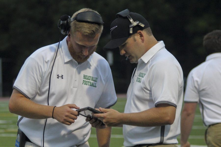 Assistant Coaches JJ Moran (left) and Adam Preciado review game footage on an iPad from the sidelines. On Friday, iPads and HUDL Sideline technology will be used to provide instant replay reviews during the game.